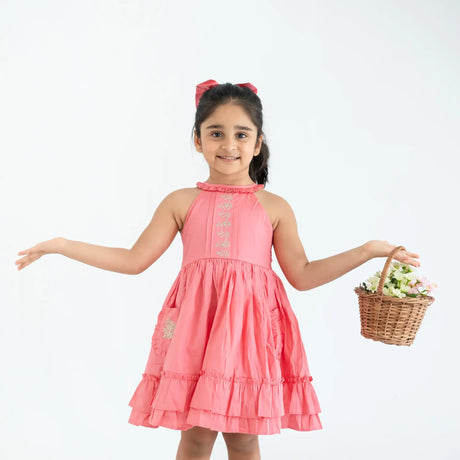 "A little girl posing in a coral embroidered cotton satin sleeveless dress with pockets."