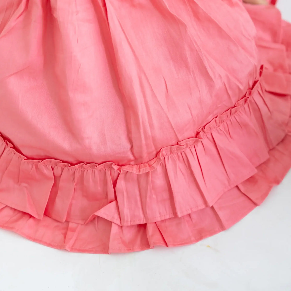 "Close-up of the ruffle details in a coral embroidered cotton satin dress."