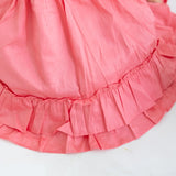 "Close-up of the ruffle details in a coral embroidered cotton satin dress."