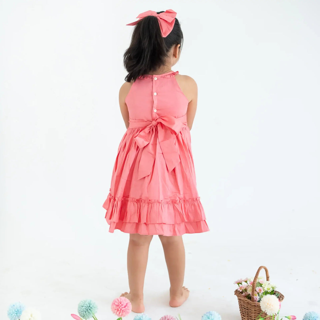 "Back pose of a girl dressed in a coral embroidered cotton satin sleeveless dress with pockets."