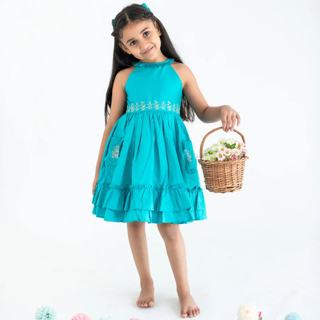 "A little girl posing in a teal embroidered cotton satin sleeveless dress with pockets."