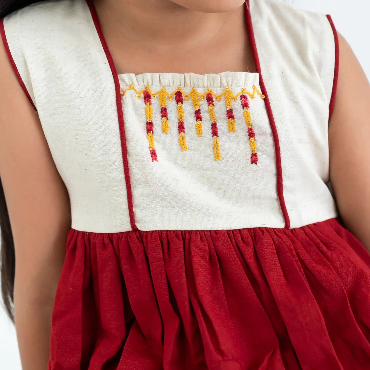 Close-up of the hand embroidery on a red sleeveless cotton dress.