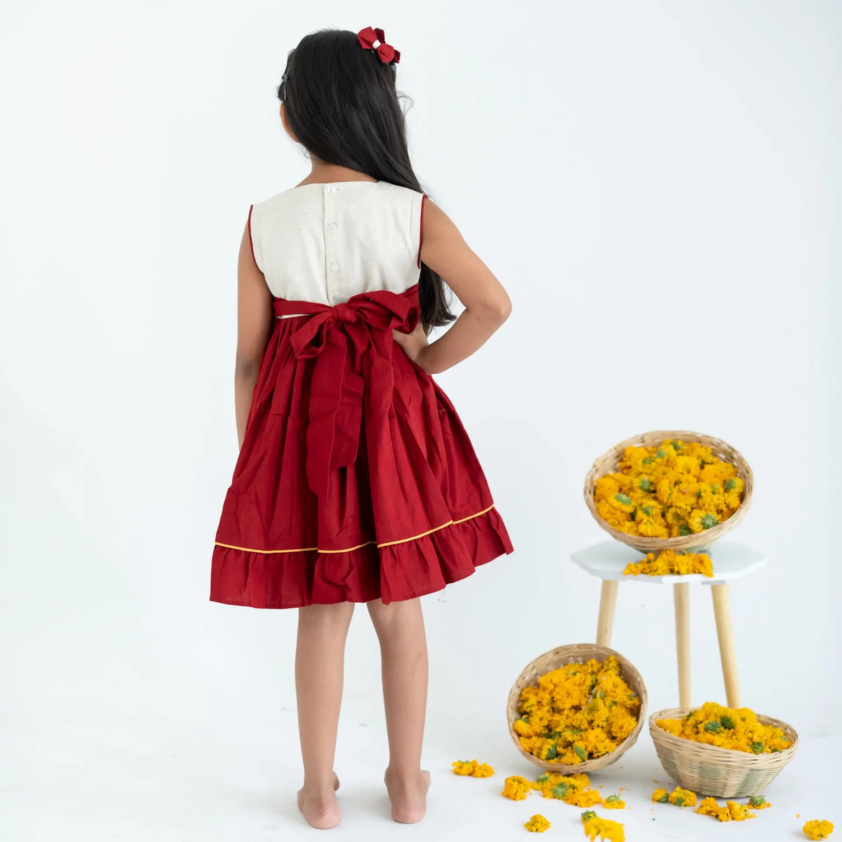 Back view of a girl wearing a red sleeveless cotton dress with hand embroidery.