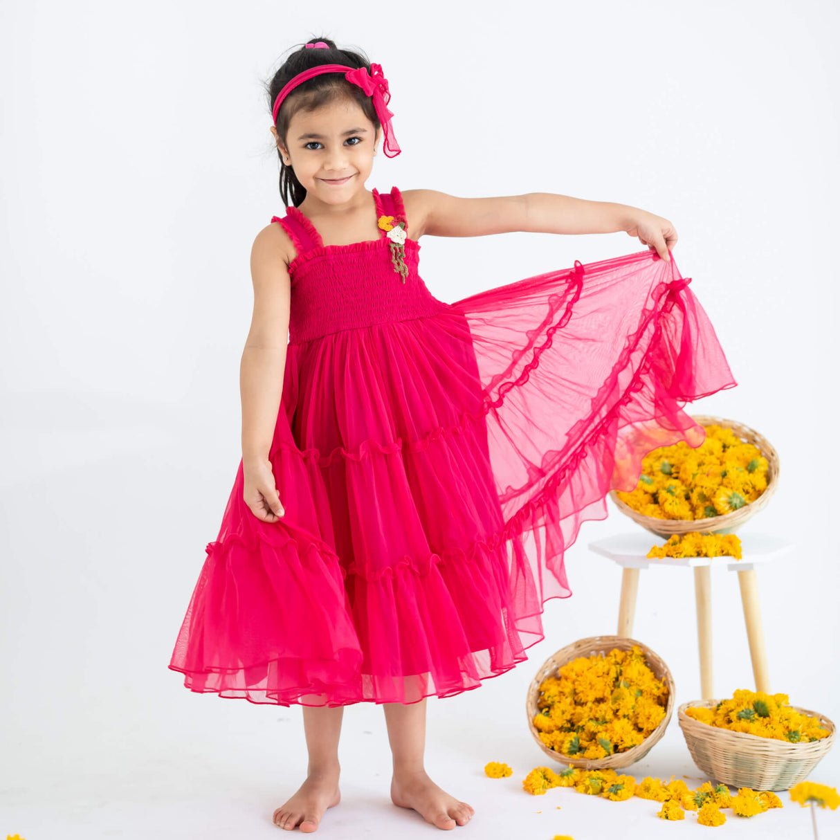 Girl posing in a pink hand-embroidered crochet nylon tulle sleeveless dress, playfully stretching the skirt.