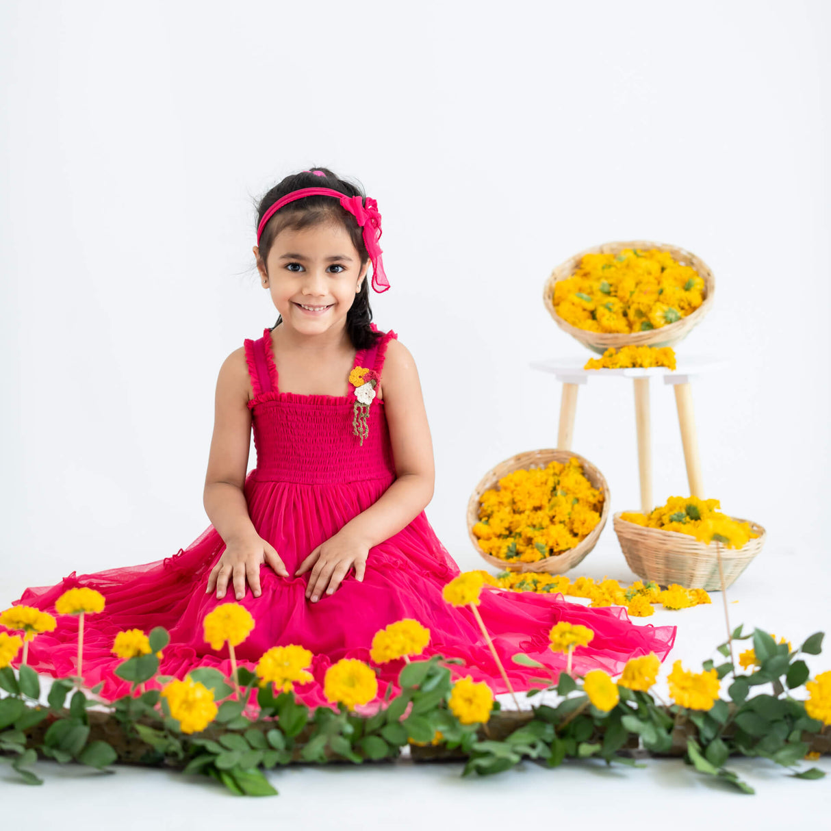 Little girl seated, wearing a pink hand-embroidered crochet nylon tulle sleeveless dress.