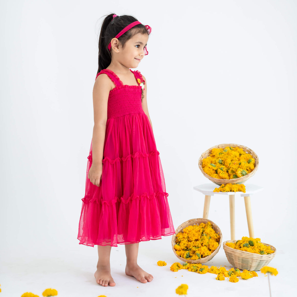 Little girl posing from the side, wearing a pink hand-embroidered crochet nylon tulle sleeveless dress.