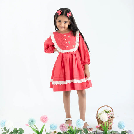 "A girl dressed in a coral pleated yoke embroidered cotton long sleeves dress."
