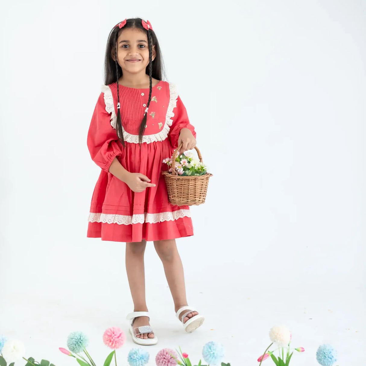 "A girl dressed in a coral pleated yoke embroidered cotton long sleeves dress."
