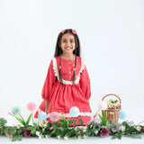 "A girl seated in a coral pleated yoke embroidered cotton long sleeves dress."