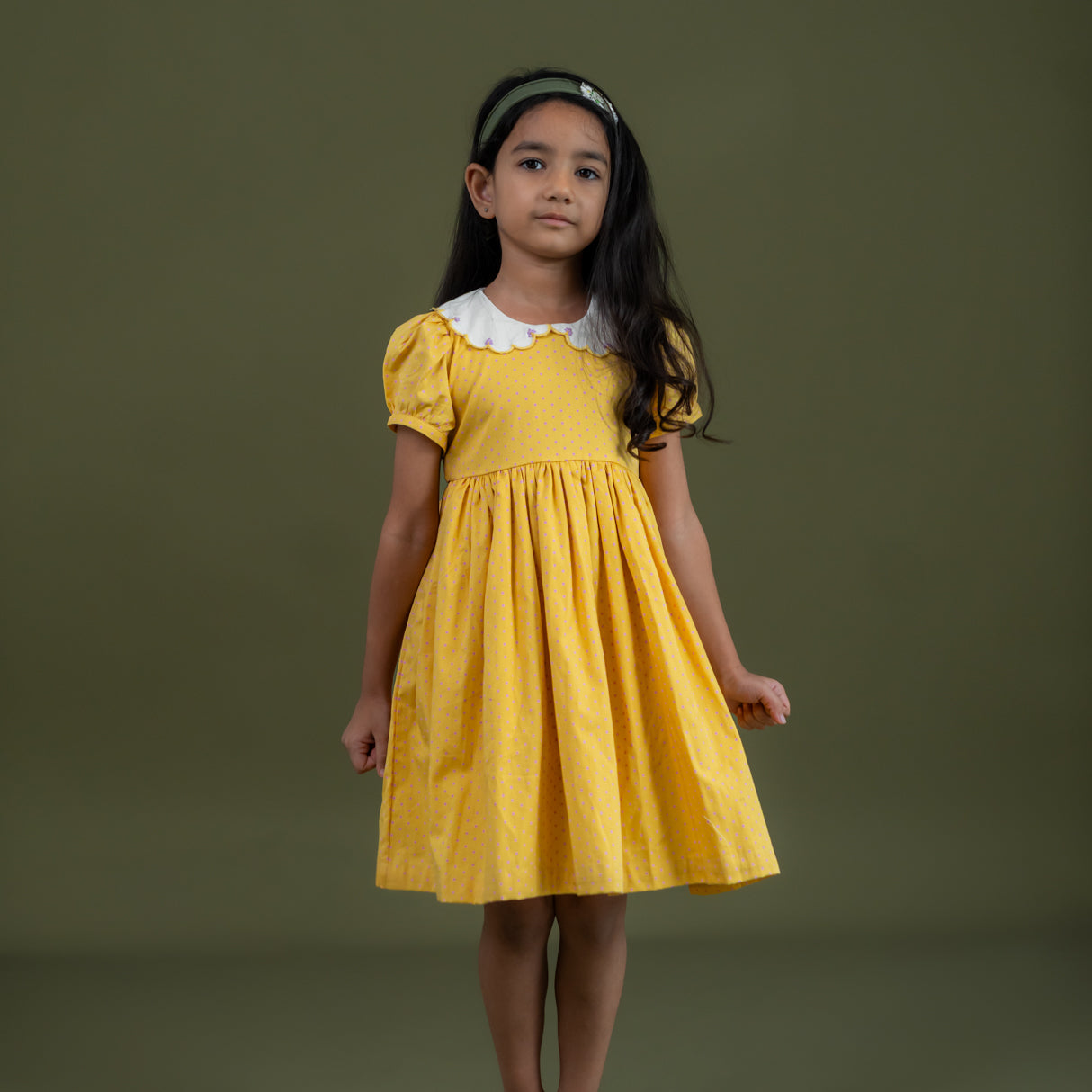 a little girl dressed in mustard dot print dress