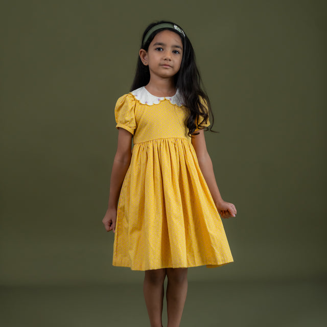 a little girl dressed in mustard dot print dress
