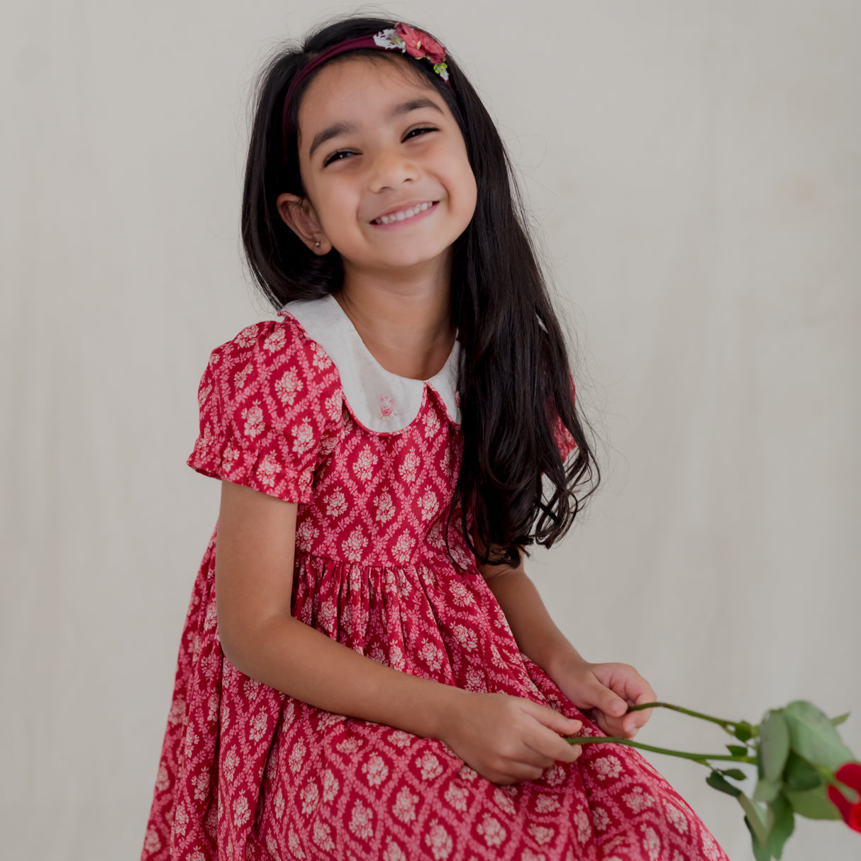a little girl seated dressed in red vintage rose print dress