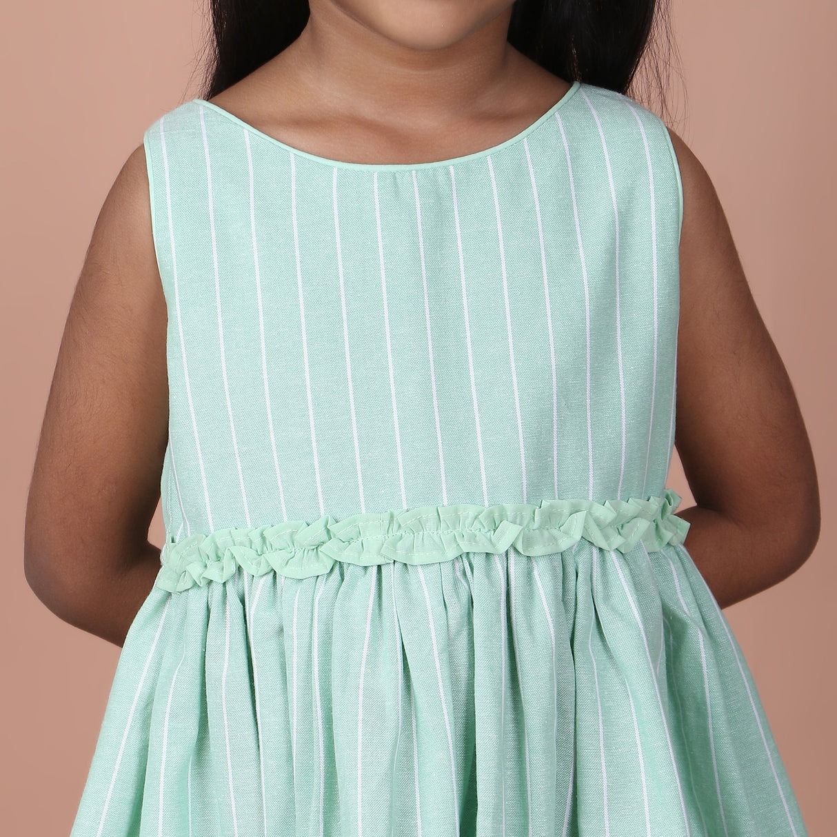 Close-up view of mint green sleeveless dress with ruffle details on waistline