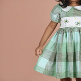 Close-up of floral embroidery smocked and green check fabric detailing on girls dress