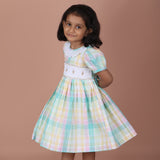 Side angle view of pastel plaid smocked dress with puff sleeves, and gathered skirt