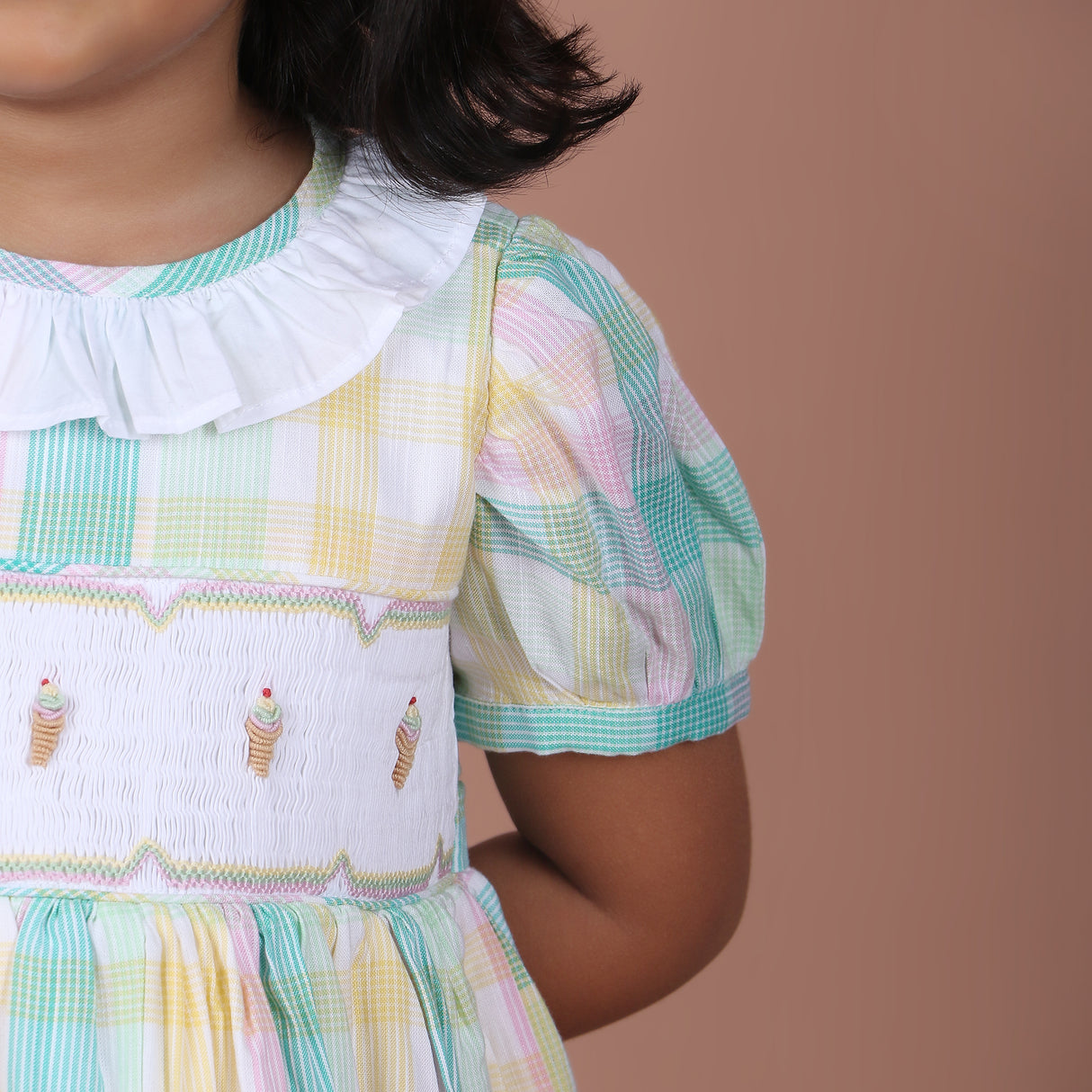 Close-up view of pastel plaid dress featuring a white ruffled collar, puff sleeves, and embroidered bodice