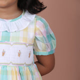 Close-up view of pastel plaid dress featuring a white ruffled collar, puff sleeves, and embroidered bodice