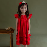 a little girl dressed in red swiss dot dress with embroidered flower button