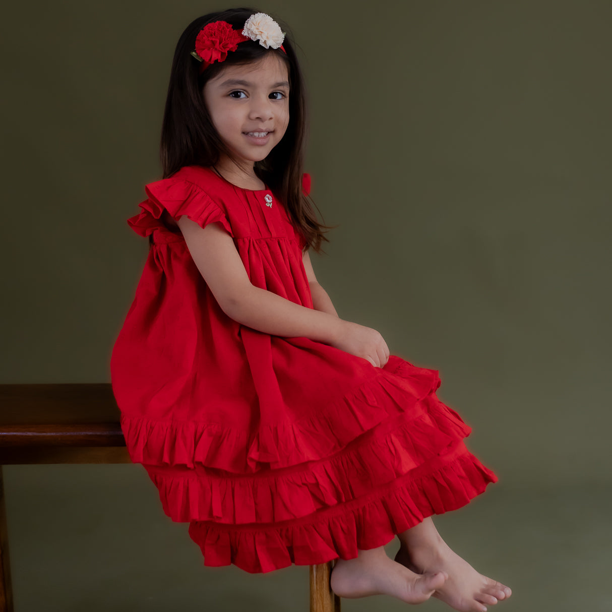a little girl seated wearing red swiss dot dress