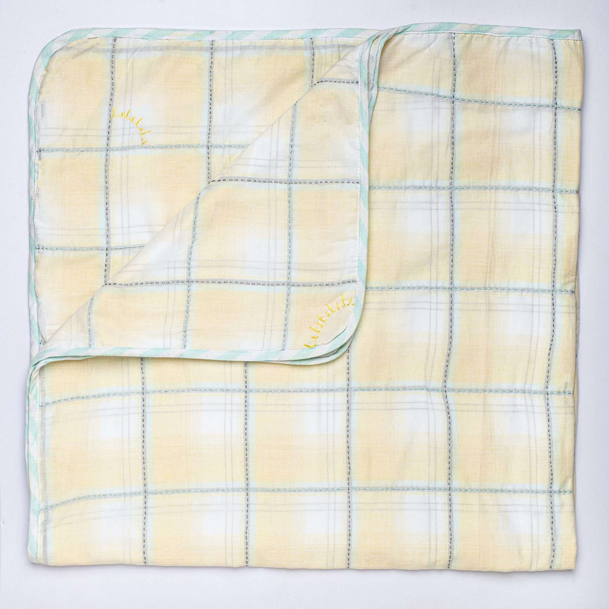 Flatlay of yellow checked blanket with hand embroidered kantha stitching between squares