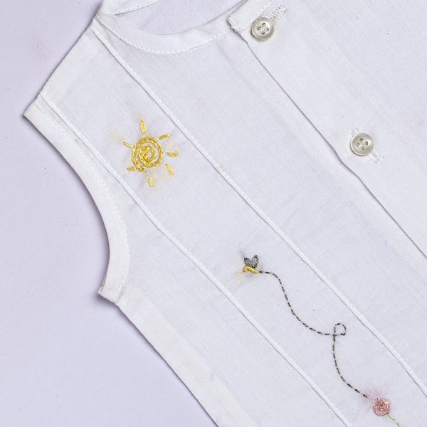 Close up of white jabla with hand embroidered flower and bee with pink plaid bloomers