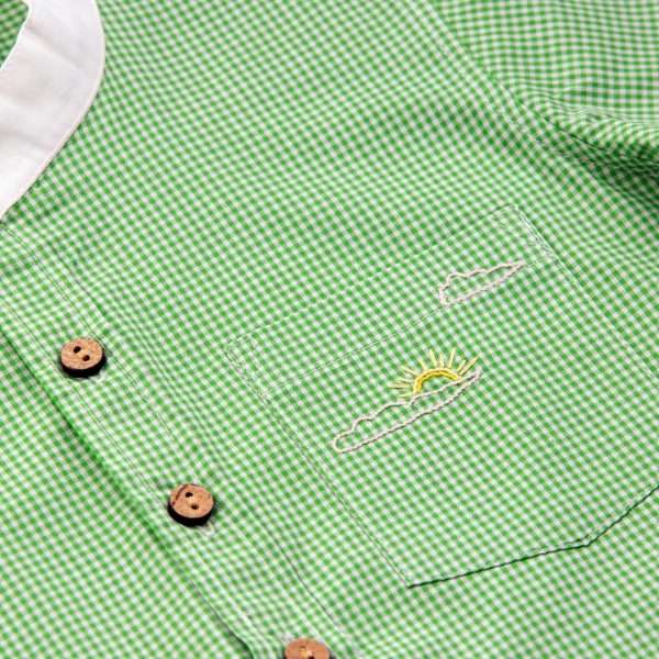 Close up of green checked shirt with small stand up collar, wood buttons, and hand embroidered sun and clouds on pocket