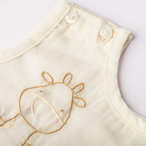 A hand embroidered giraffe and 2 shoulder buttons are visible on a tan infant vest