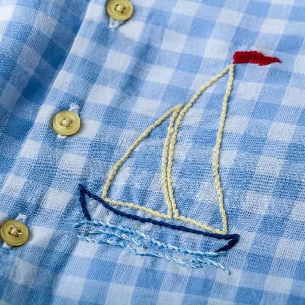 Close-up of blue check onesie with hand embroidered sailboat and yellow piping trims