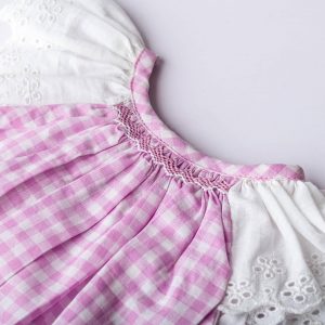 Close-up flatlay image of the hand smocked neckline and lacy flutter sleeves of gingham onesie for baby girls