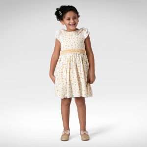 Girl smiles in a white dress that has yellow smocking