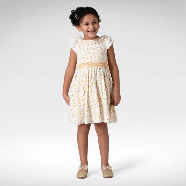 Girl smiles in a white dress that has yellow smocking
