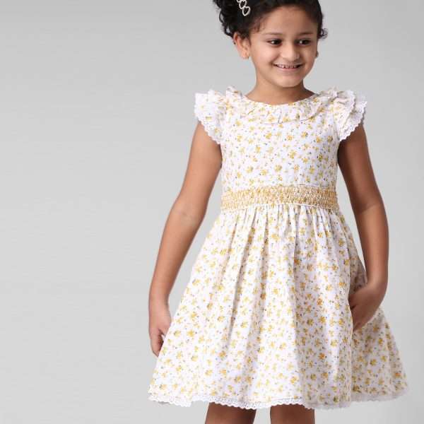 A little girl in swiss-dot floral dress with hand-smocked waistline and eyelet lace trims in flutter sleeves and hem