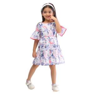 A little girl with a cheeky smile wearing swiss dot pink and blue floral printed cotton dress with bell sleeves