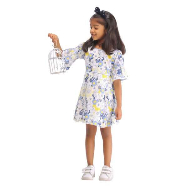A little girl in swiss dot blue floral printed cotton dress with boat neck and elasticated shirring on bell sleeves