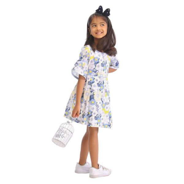 A little girl in swiss dot blue floral printed cotton dress with boat neck and elasticated shirring on bell sleeves