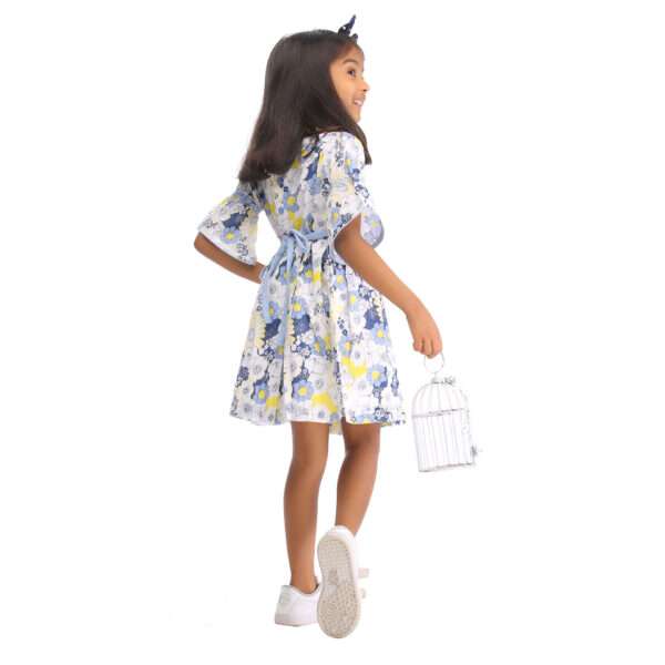 Rear image of a little girl in swiss dot blue floral printed cotton dress with elasticated shirring on bell sleeves