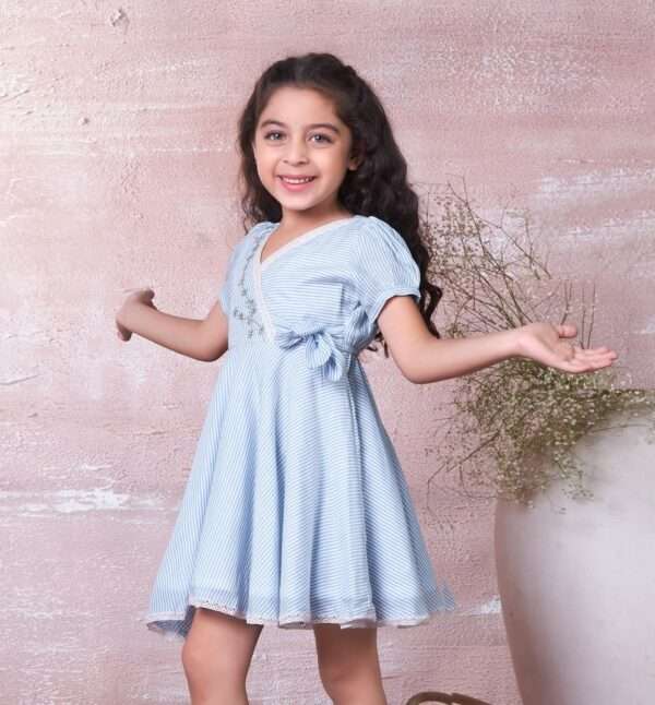 A girl in blue striped cotton dress with delicate crochet-style lace trim, floral hand-embroidery and faux cross-over