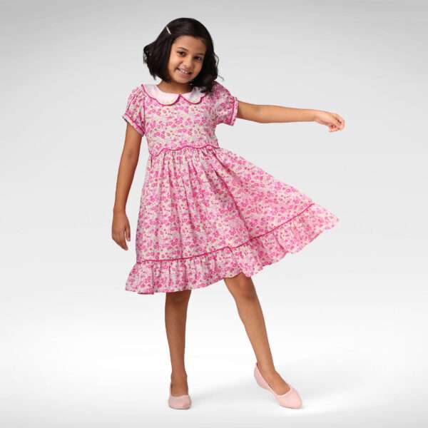 A little girl in pink floral dress with scalloped waistline, hand embroidered collar, puff sleeves and ruffled hem