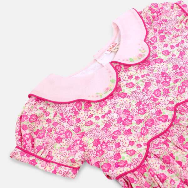 Close up of pink floral dress with scalloped waistline and collar with hand embroidery and ruffled hem