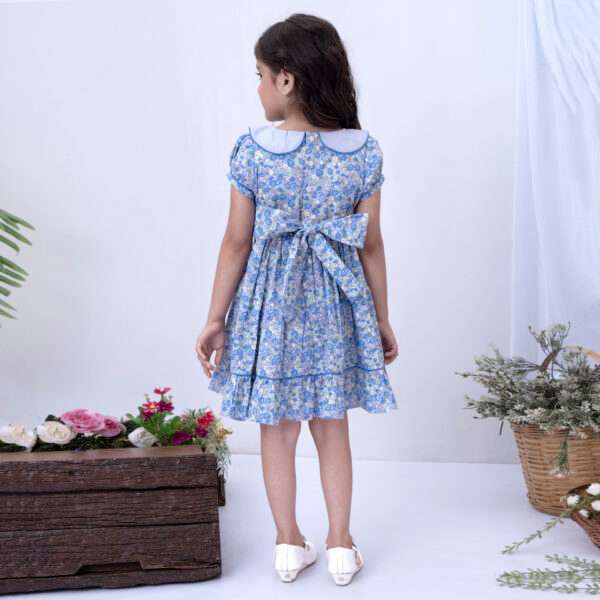 Back view of a girl wearing a floral print dress in blue with a ruffle hem and back ties