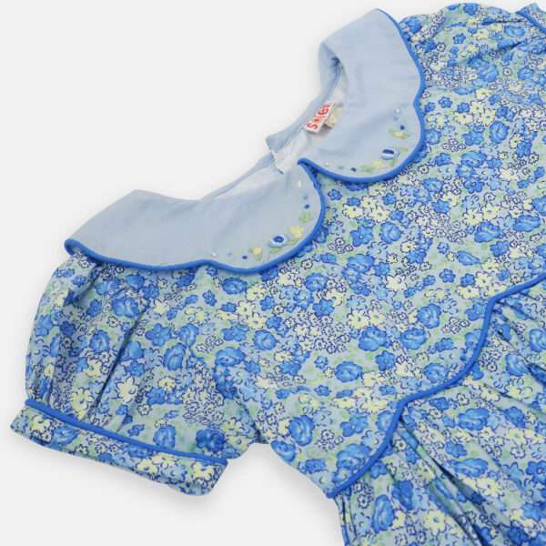 Close up of blue floral dress with scalloped waist and collar, and hand embroidered flowers on collar and ruffled hem
