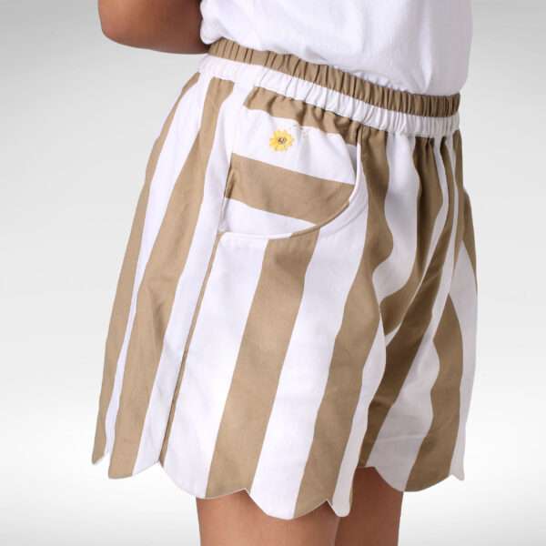 Girl wearing scallop hem shorts in tan and white stripe with small floral pocket embroidery