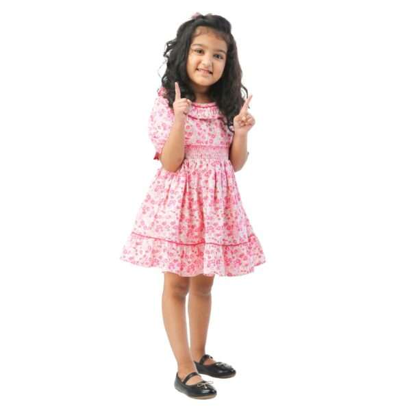 A little girl in floral printed cotton dress with a hand smocked waistline, puff sleeves, ruffled collar as well as hem