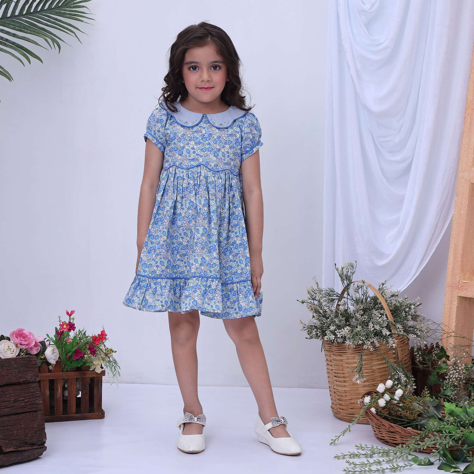 A little girl in blue floral dress with scalloped waistline and collar, hand embroidered flowers on collar, ruffled hem