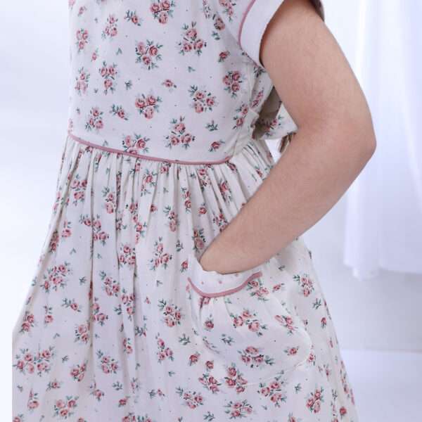 A girl wearing ivory floral printed dress with a hand in the pocket that has hand embroidered details