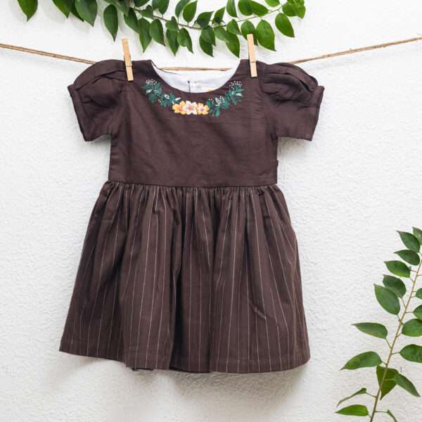 A girl wearing brown twill girls dress featuring a broad floral neckline embroidery