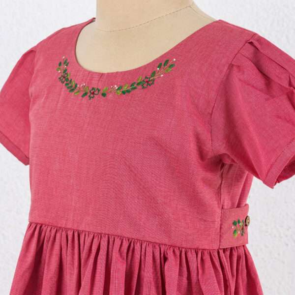 Close up of red chambray dress with hand embroidered neckline, puff sleeves, and pleated hem