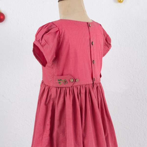 Side view of red chambray girls dress and side tabs with small cherry embroidery and wood buttons