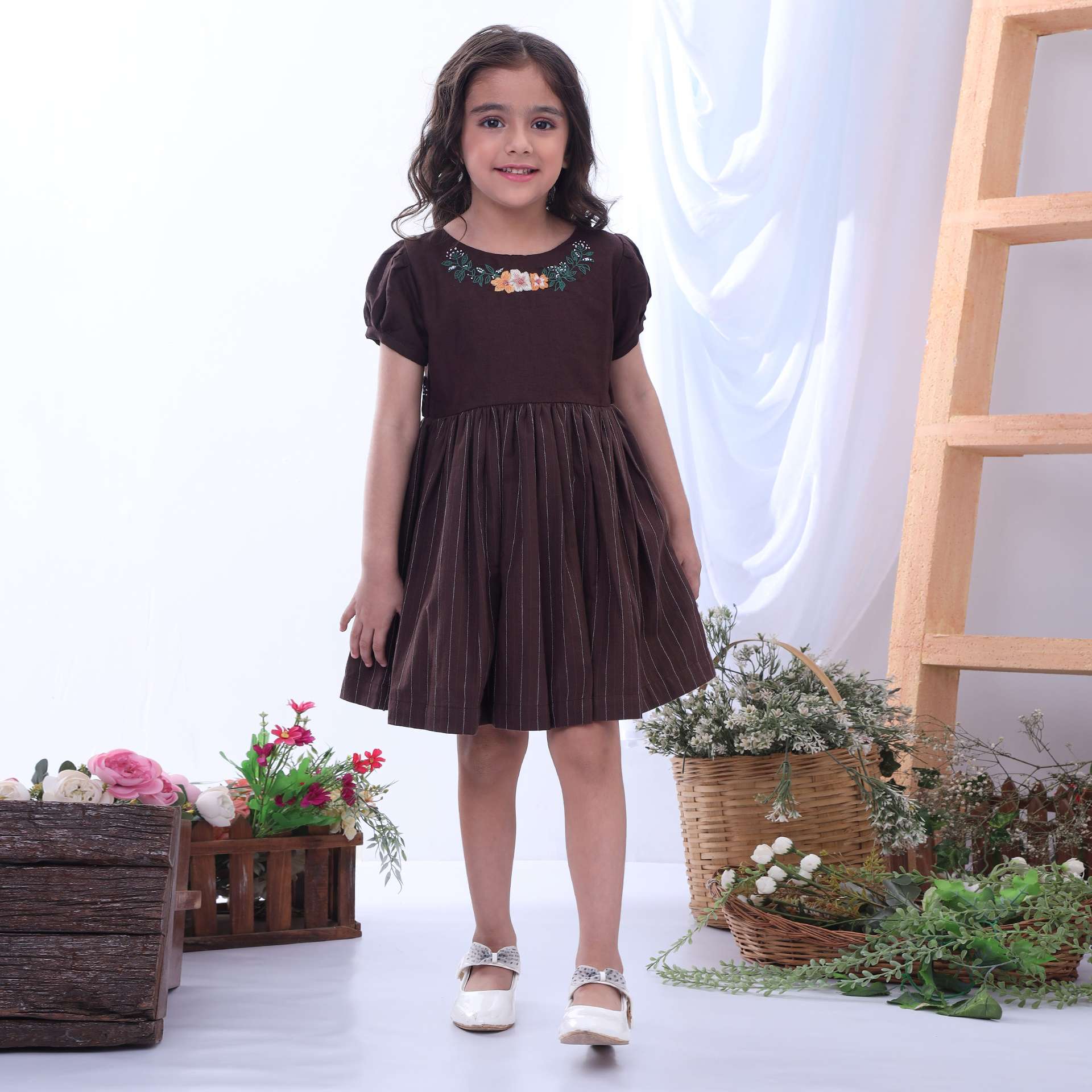 Girl posing in brown twill girls dress featuring a broad floral neckline embroidery