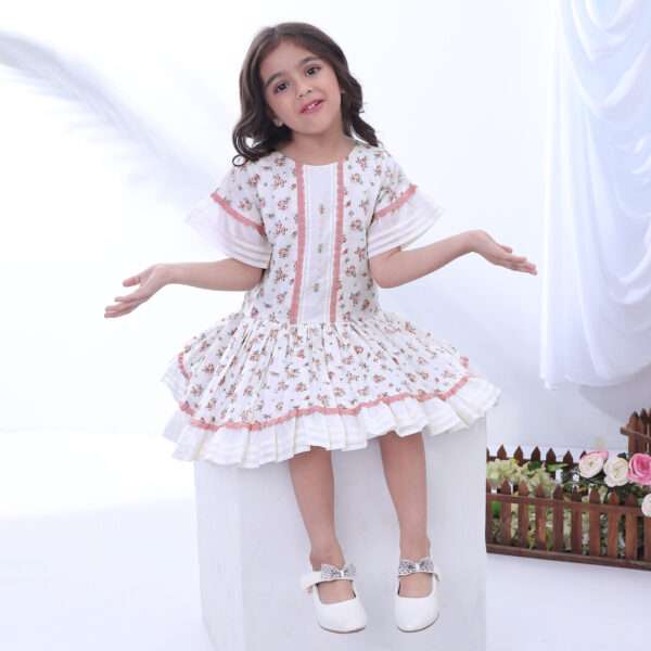A girl posing in ivory floral printed cotton dress with a drop waist, dusty pink lace trims and hand embroidered bodice
